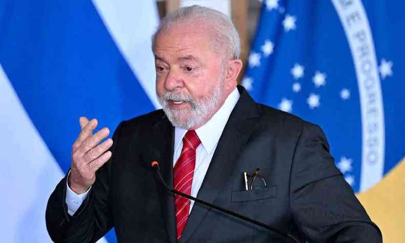 Lula falando ao microfone diante de uma bandeira do Brasil