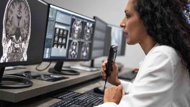 Uma pesquisadora olhando para uma tomografia do crebro no computador e falando em um ditafone