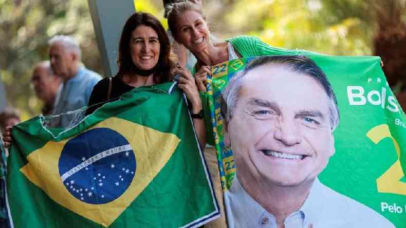 Duas mulheres sorrindo e mostrando para a cmera bandeira do Brasil e imagem de Bolsonaro