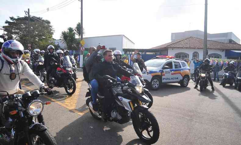 Pilotando uma motocicleta e com homem na garupa, Bolsonaro participa de motociata em Juiz de Fora