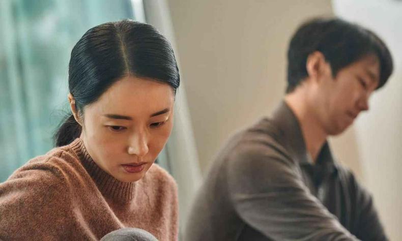 Lee Jung-hyun e Park Hae-il em cena do sul-coreano 'Decisão de partir', cotado para o prêmio(foto: Moho Film/divulgação) Atriz Lee Jung-hyun olha para baixo, com semblante triste, com ator Park Hae-il ao fundo em cena do filme Decisão de partir