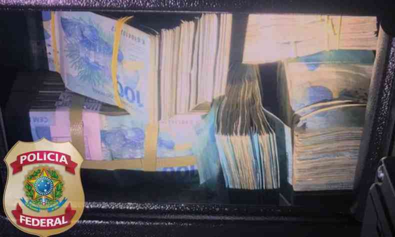 Na foto, Maços de dinheiro apreendidos dentro de um cofre, durante a Operação 'Habeas Pater', ao lado de um logo da PF