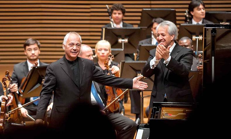 O pianista Jean Louis Steuerman foi convidado pelo maestro Fabio Mechetti para se apresentar na Sala Minas Gerais(foto: André Fossati/divulgação) Sorridente, o pianista Jean Louis Steuerman abre o braço em direção ao maestro Fabio Mechetti, que o aplaude, tendo músicos da Orquestra Filarmônica ao fundo