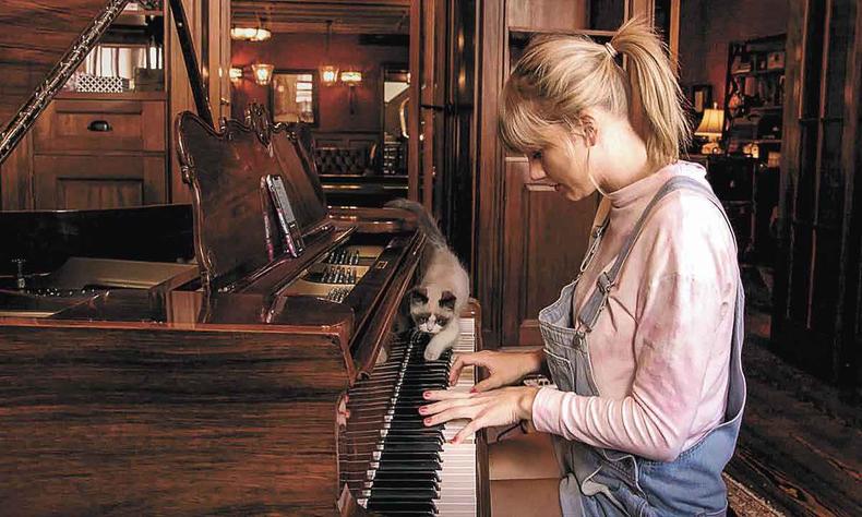 Taylor Swift toca piano, vestindo roupas caseiras, e tem um gato caminhando no teclado