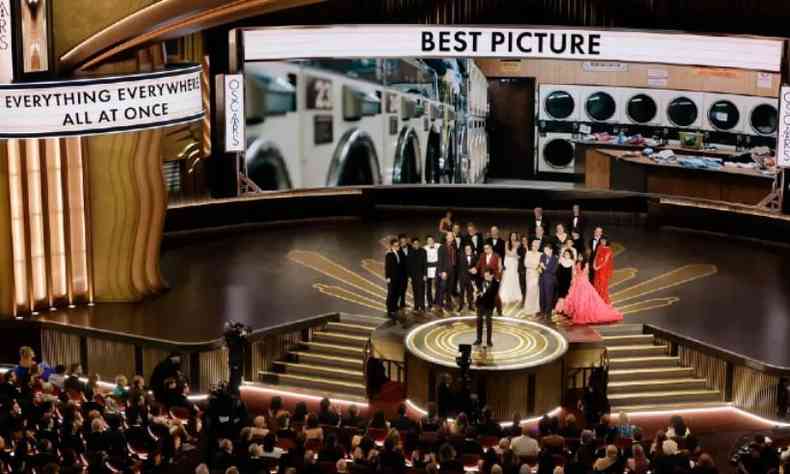 Equipe de 'Tudo em Todo o Lugar ao Mesmo Tempo' reunida no palco do Oscar. Ao fundo, se l 'Best Picture' e 'Everything Everywhere All At Once'