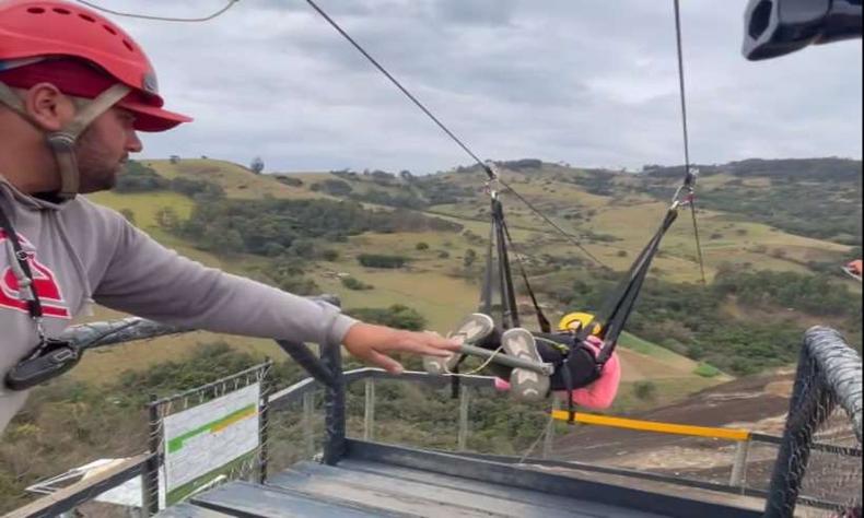 mulher em uma tirolesa, ao fundo dá para ver a paisagem