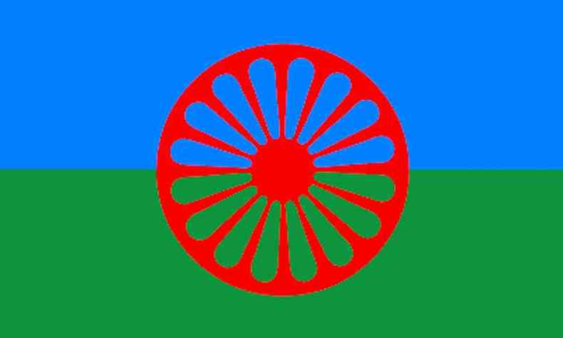 Bandeira Cigana, dividida ao meio no sentido horizontal, sendo azul na parte de cima e e verde na parte de baixo. Ao centro se encontra um smbolo circular que lembra uma flor vermelha