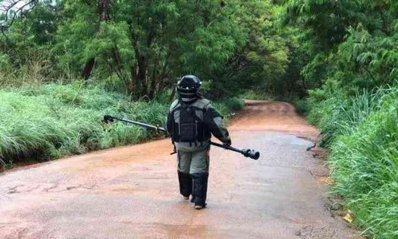 Policial com roupa camuflada e almofadada, capacete e colete  prova de balas caminha em estrada de terra em meio a mata