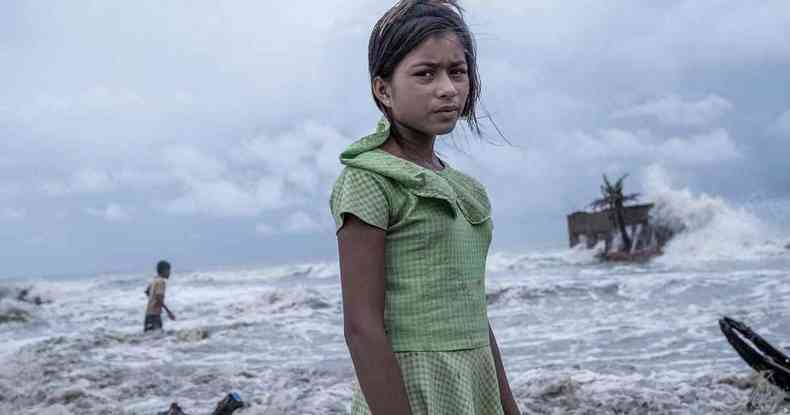 Uma garota de 11 anos com um vestido, um olhar desolado e um mar agitado s suas costas
