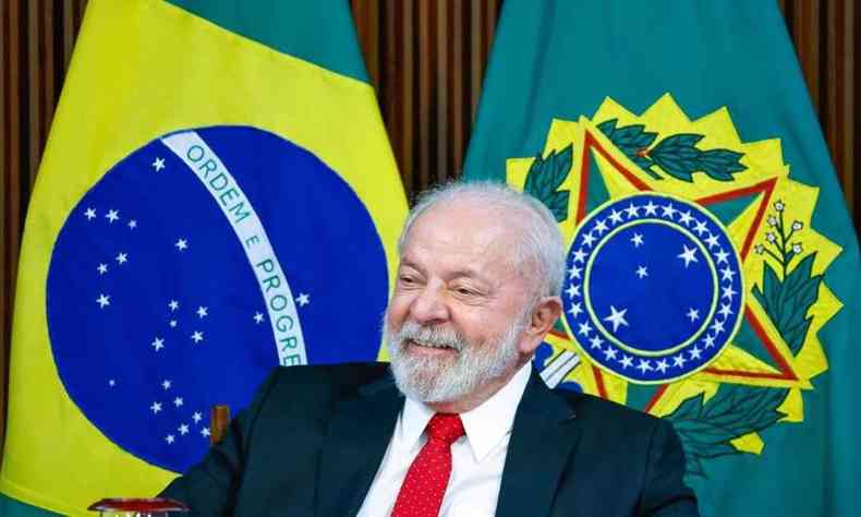 Lula sorrindo com a bandeira brasileira ao fundo