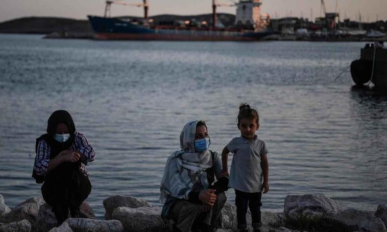 Duas mulheres com lenos na cabea e uma menina; ao fundo o mar e um navio no porto