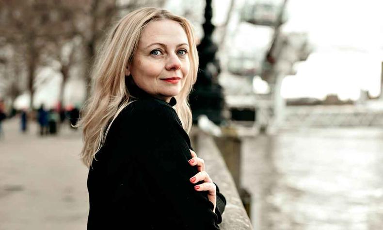 Nara Vidal vive em Londres e planeja livro dedicado às personagens femininas de Shakespeare (foto: Bruna Casotti/divulgação) Escritora Nara Vidal sorri, olhando para a câmera, com os cotovelos na murada às margens de um rio, em dia nublado