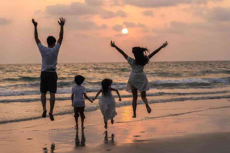 Familia composta por um casal e dois filhos pulando, de frente para o mar, durante o por do sol