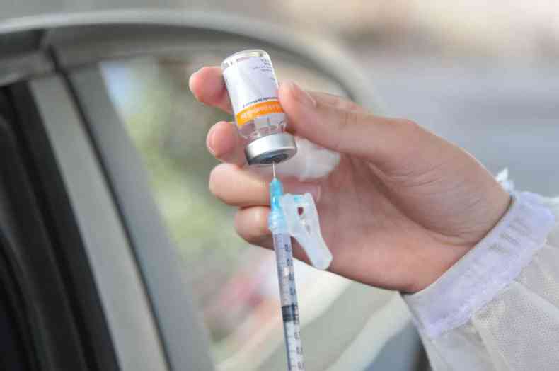 Profissional de saúde insere seringa em frasco de vacina contra a COVID-19