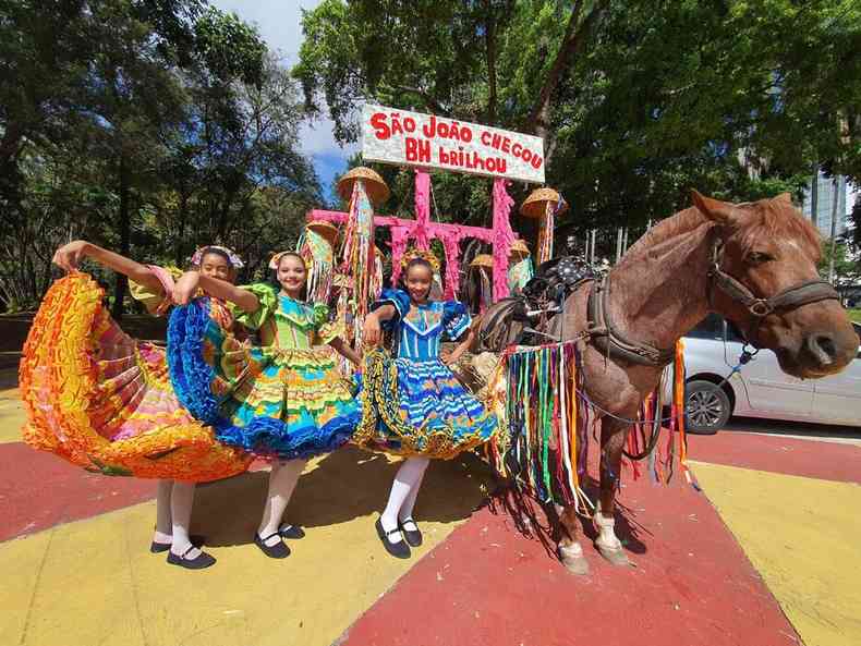 Trs meninas vestidas de roupas de festa junina ao lado de uma carroa enfeitada