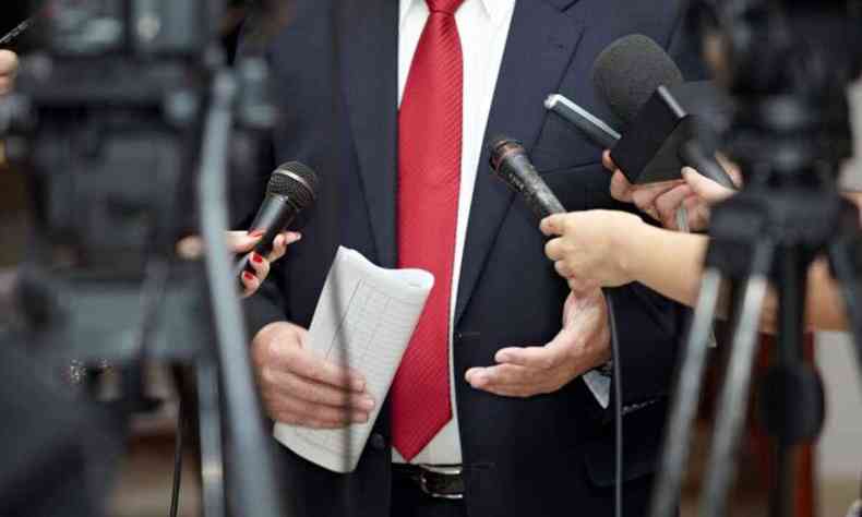 Homem de terno e gravata vermelho em uma entrevista coletiva