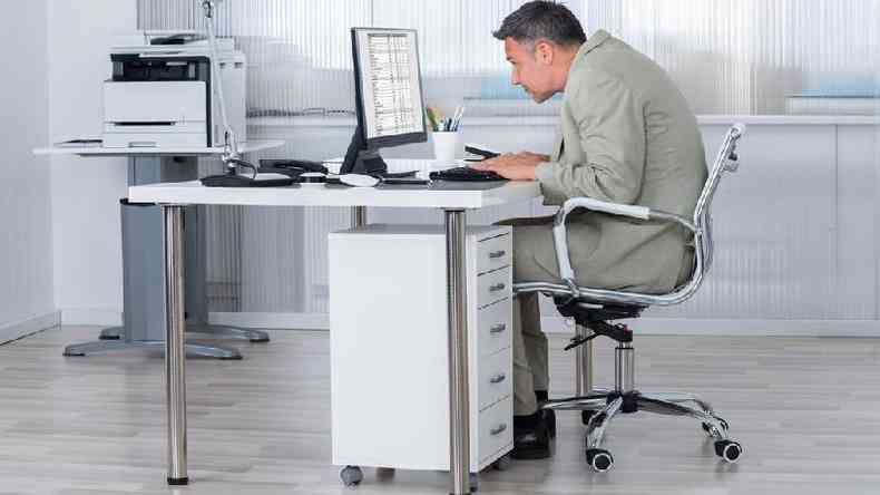 Homem trabalhando sentado e com a postura encurvada diante do computador