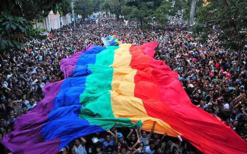 Manifestantes da Parada LGBT encobertos pela bandeira nas cores do arco-ris