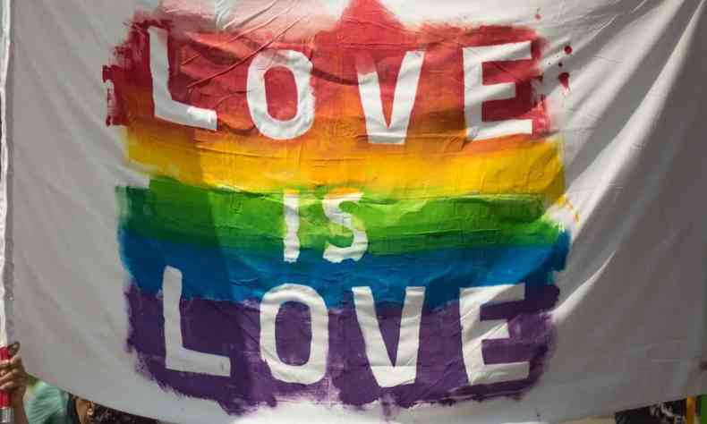 Bandeira pintada com as cores do arco-íris escrito em branco: Love is love