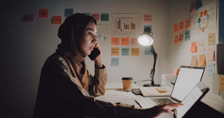 Mulher falando no celular enquanto olha para tela de computador em sala de estudos ou trabalho