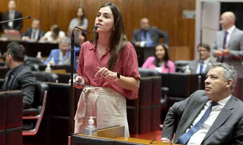 Lohanna  um mulher jovem, branca, tem cabelos escuros compridos; na foto, ela fala o microfone