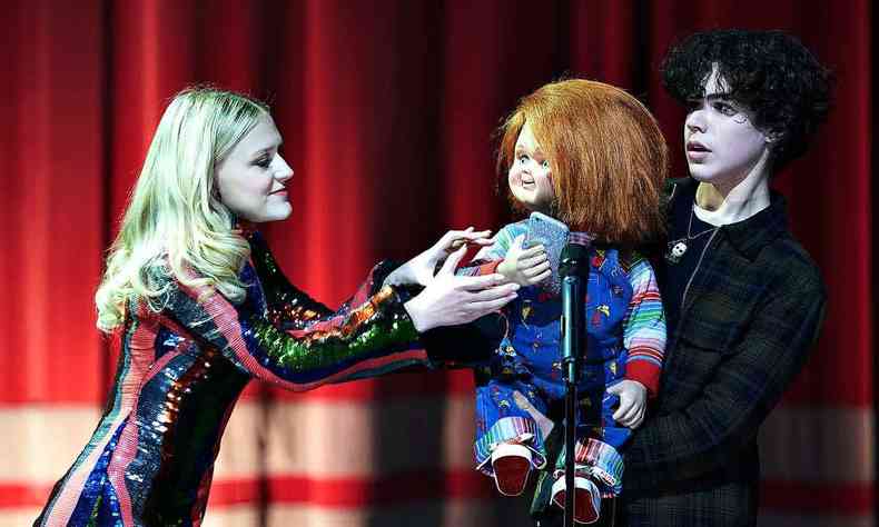 Mulher tenta pegar o boneco Chucky dos braos do adolescente que  seu dono, num palco, em frente a um microfone