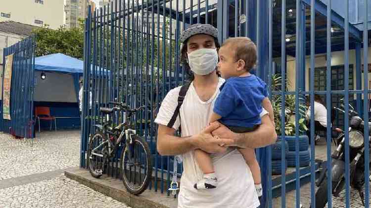 Renan Bidutti de mscara com o filho no colo, em frente a posto de sade