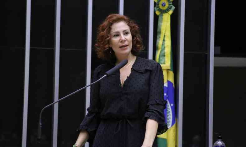Carla Zambelli na plenria da Cmara dos Deputados. Ela  uma mulher branca de cabelos ruivos. Ao fundo uma bandeira do Brasil