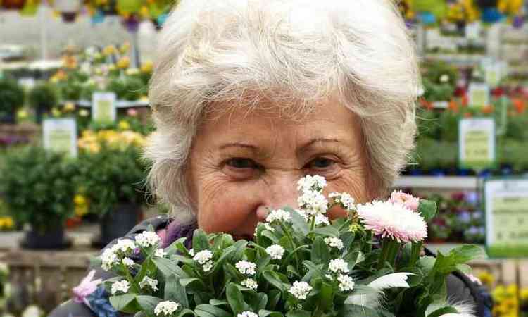idosa sorrindo, atrs de um arranjo de flores, que est na frente do seu rosto