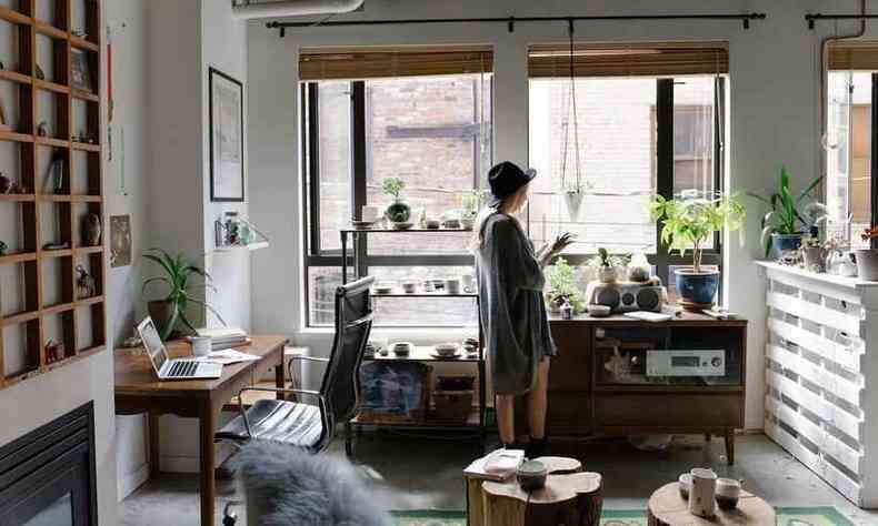 Mulher de chapu e vestido, em p, na sala de casa transformada em home office
