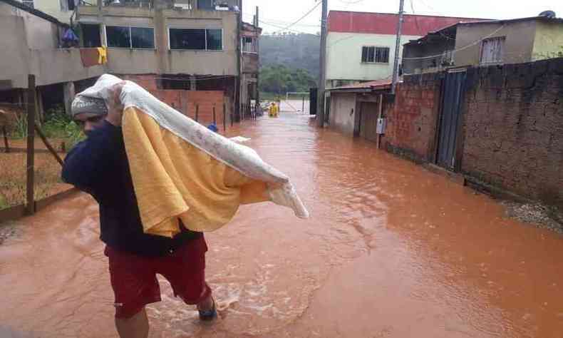 Homem carrega colcho em meio  enchente 