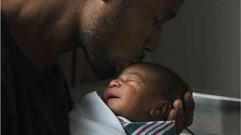 Homem negro segura bebê e beija sua testa
