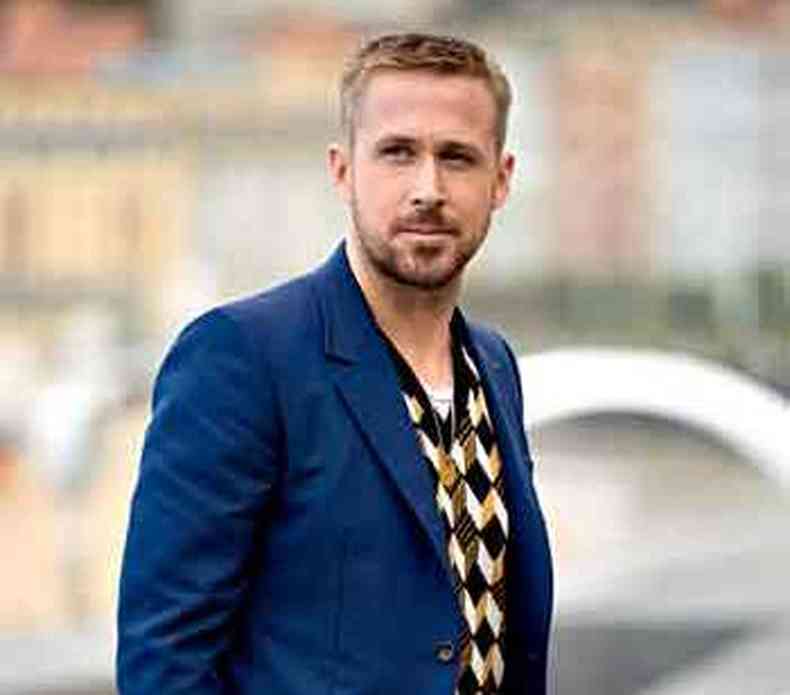 De terno azul escuro e pulver quadriculado, com as mos nos bolsos, ator Ryan Gosling olha para o horizonte