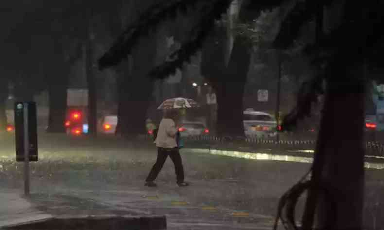 Mulher atravessa avenida de BH durante chuva 