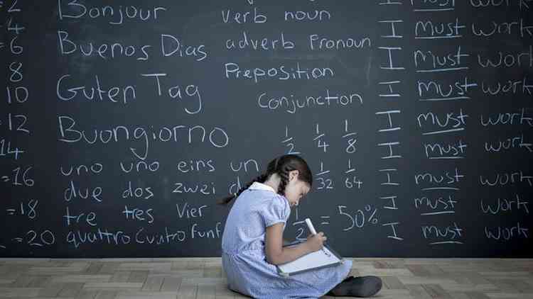 Menina escrevendo em caderno em frente a lousa com palavras em vrias lnguas
