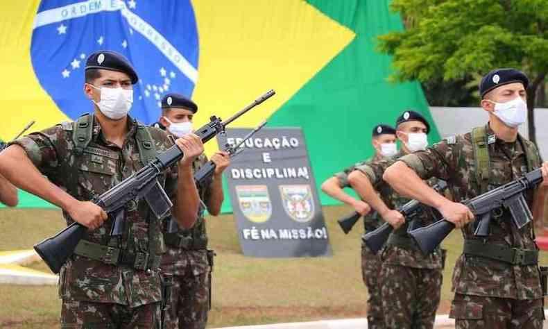 Soldados do exrcito fazem atividade com armas nas mos; ao fundo, uma bandeira do Brasil