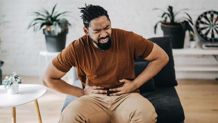 Homem com mos na barriga e rosto demonstrando desconforto; ele est sendado em uma sala de estar