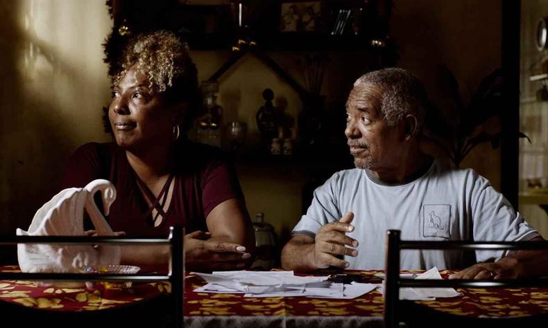 Atores Carlos Francisco e Rejane Faria esto sentados  mesa e olham para o lado em cena do filme Marte Um