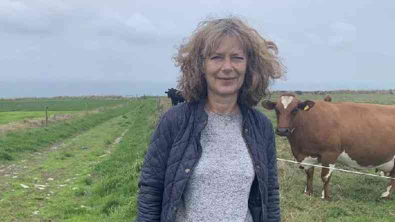 Uma mulher branca e idosa em frente a um pasto de vacas