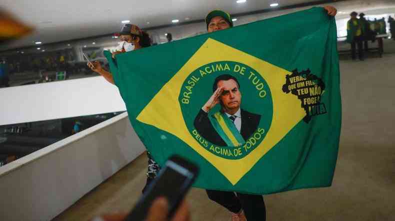 Mulher segura bandeira com rosto de Bolsonaro dentro do Planalto invadido