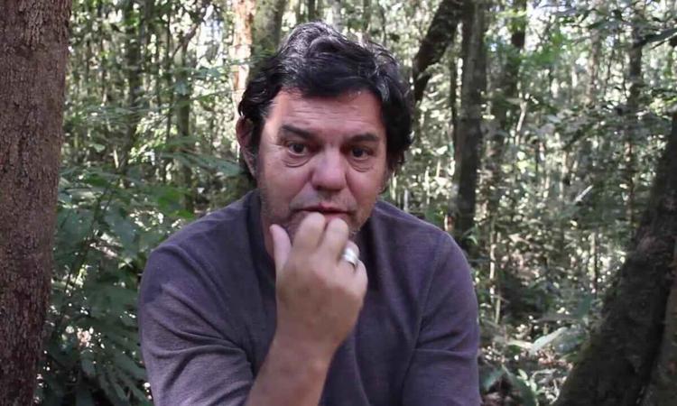 Ator Chico Pelcio, sentado em cadeiras de teatro, olha para a cmera