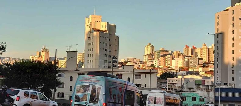 Avenida com carros, prdios ao fundo iluminados pelo sol e cu azul.