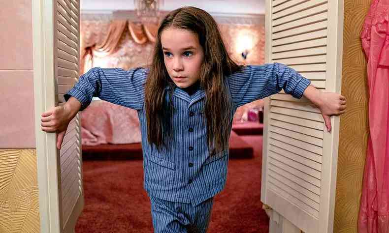 Alisha Weir de pijama abre a porta do quarto e ao fundo se v cama de casal, no filme Matilda: O musical