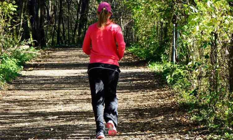 mulher agasalhada correndo em uma trilha, em meio  natureza
