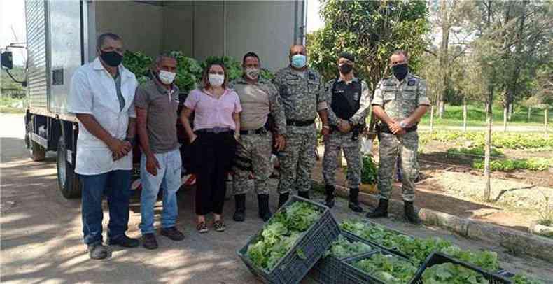 policiais e integrantes do projeto posam para foto diante de carregamento de hortalias