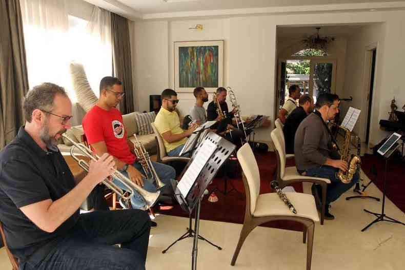 Músicos da Happy Feet Jazz Band ensaiam com seus instrumentos, sentados em cadeiras em sala ampla