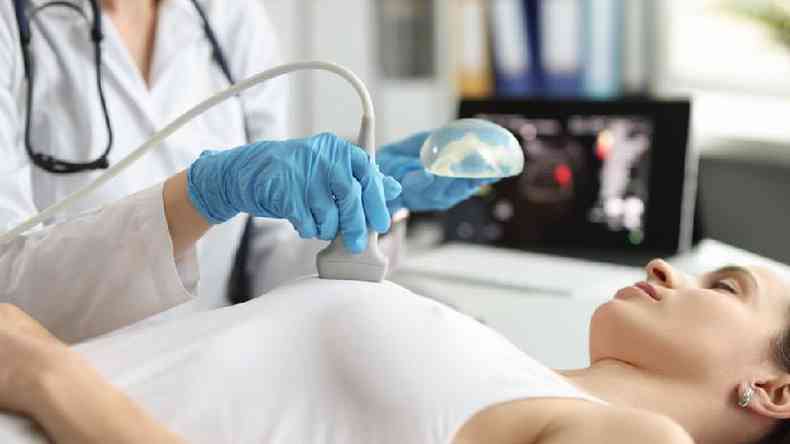 Profissional da saúde segura prótese mamária de silicone enquanto faz ultrassom em mulher