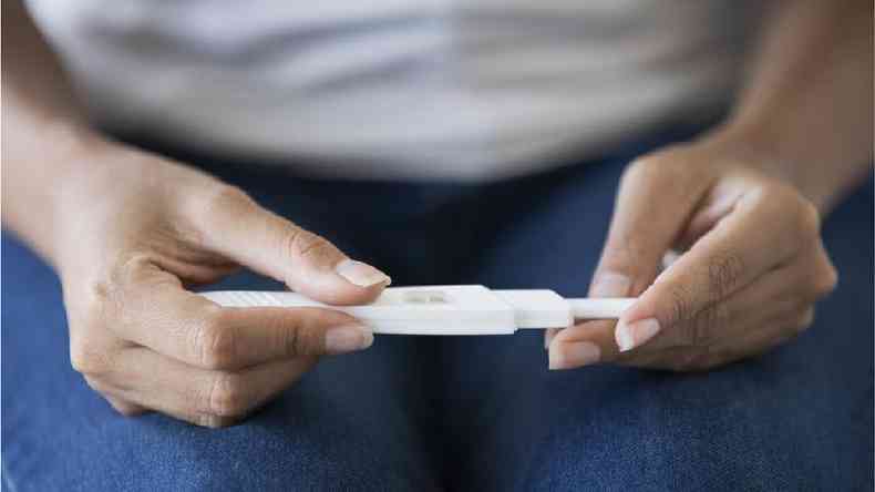 Duas mãos seguram um aparelho que parece ser um teste de gravidez