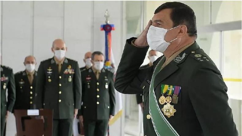 Fotografia colorida mostra em primeiro plano homem branco de meia idade com mscara, cabelo preto curto e uniforme militar batendo continncia; ao fundo h outros homens brancos de uniforme militar