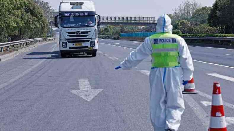 Policial paramentado com roupas anticovid faz sinal para um caminho em uma estrada parar